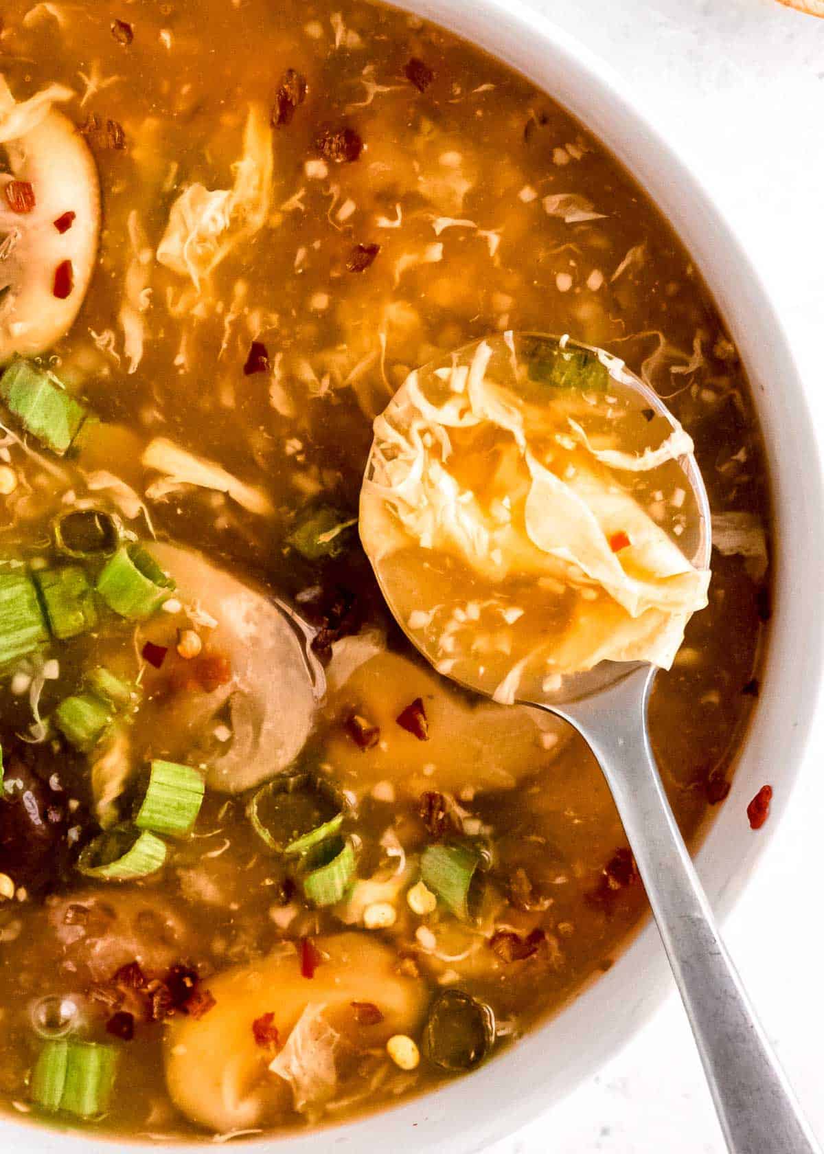 hot and sour soup in white bowl with spoonful of soup in foreground