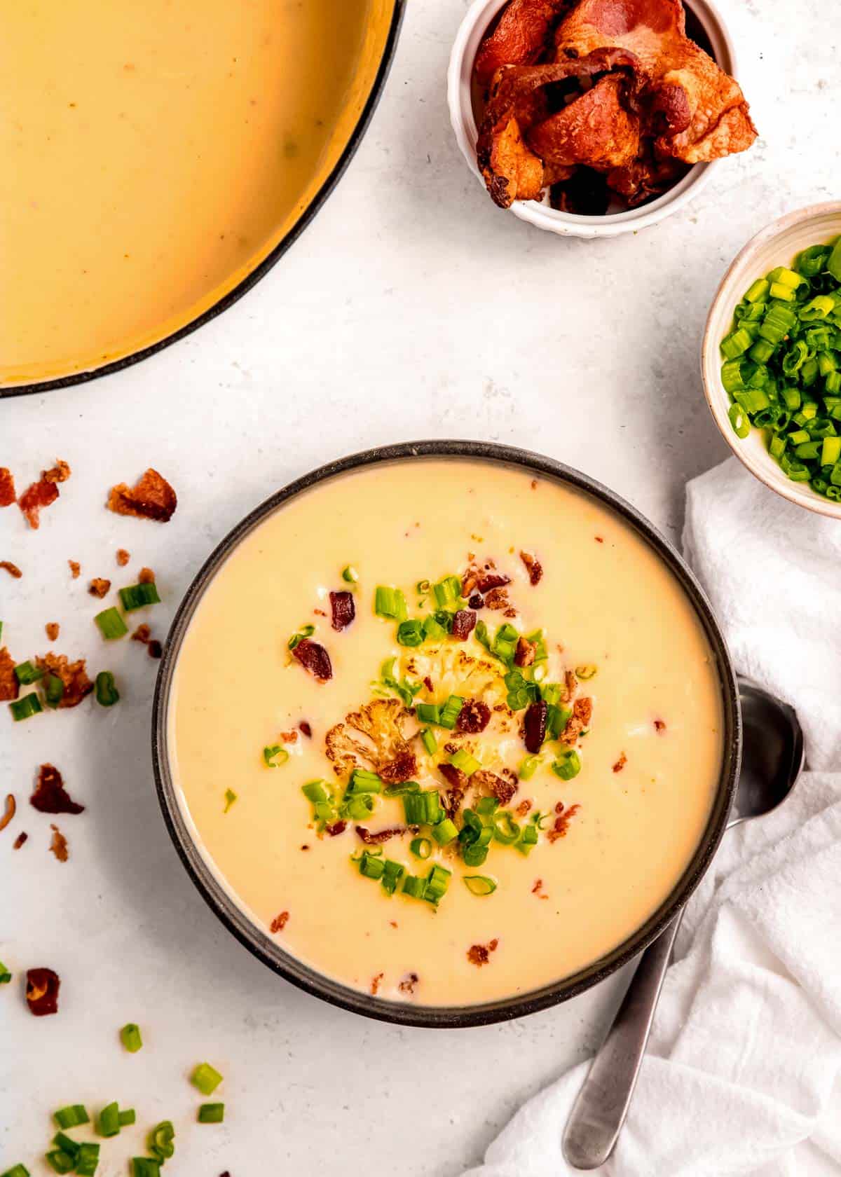 overhead image of loaded cauliflower soup in black bowl on white table