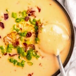 close up overhead image of loaded cauliflower soup in black bowl with silver spoon