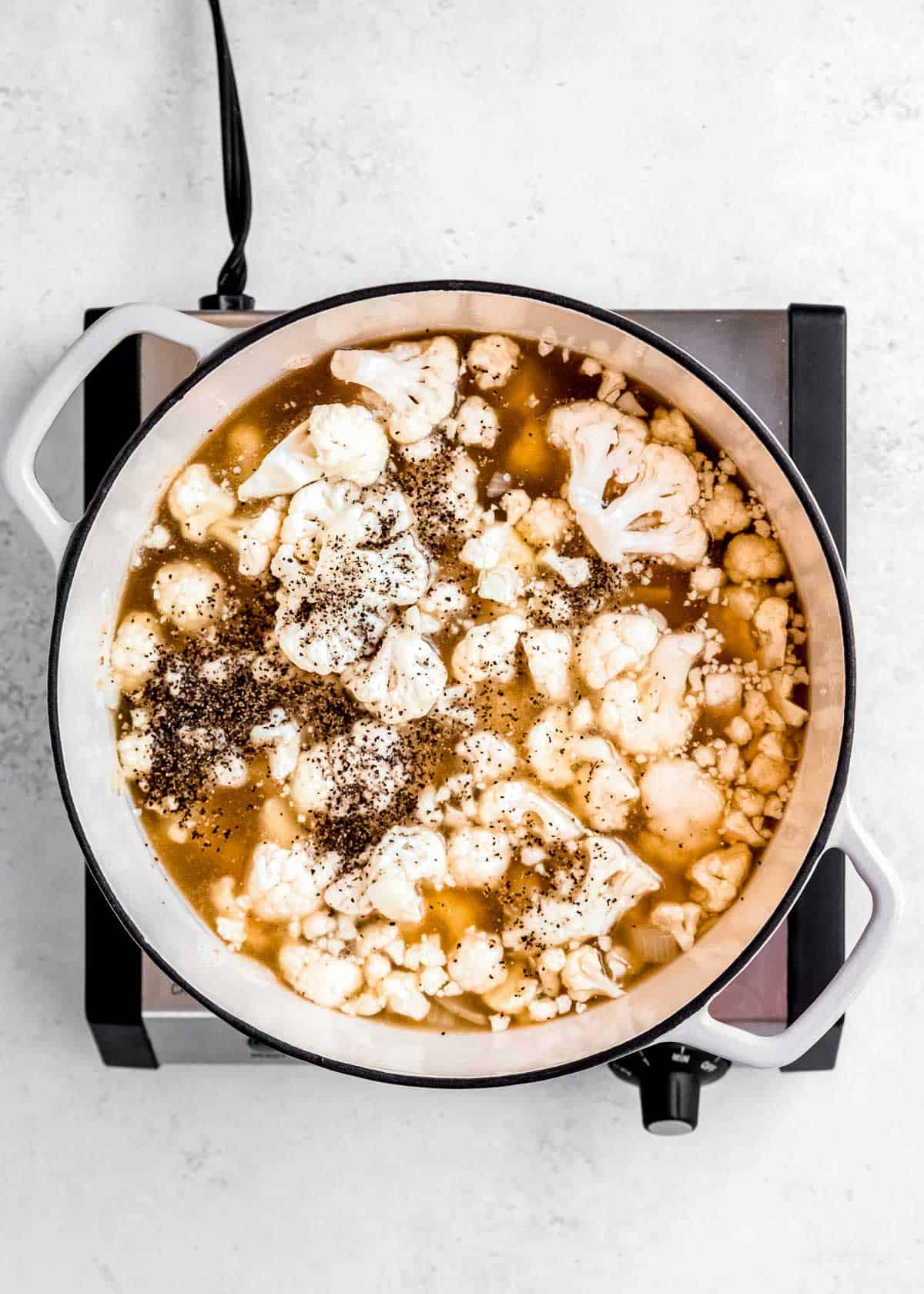 chicken broth and cauliflower being added dutch oven