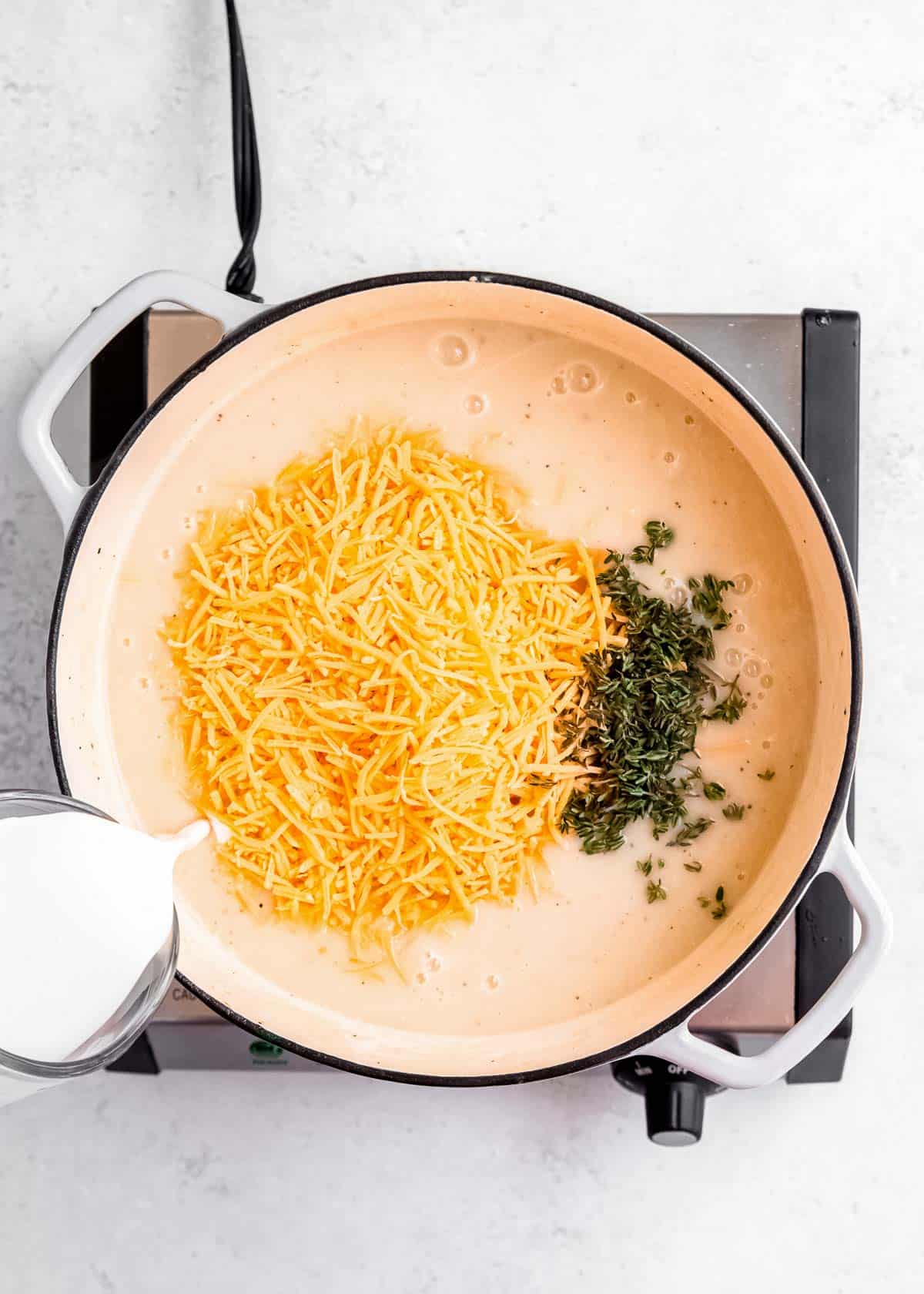 cheddar cheese being added to loaded cauliflower soup in dutch oven