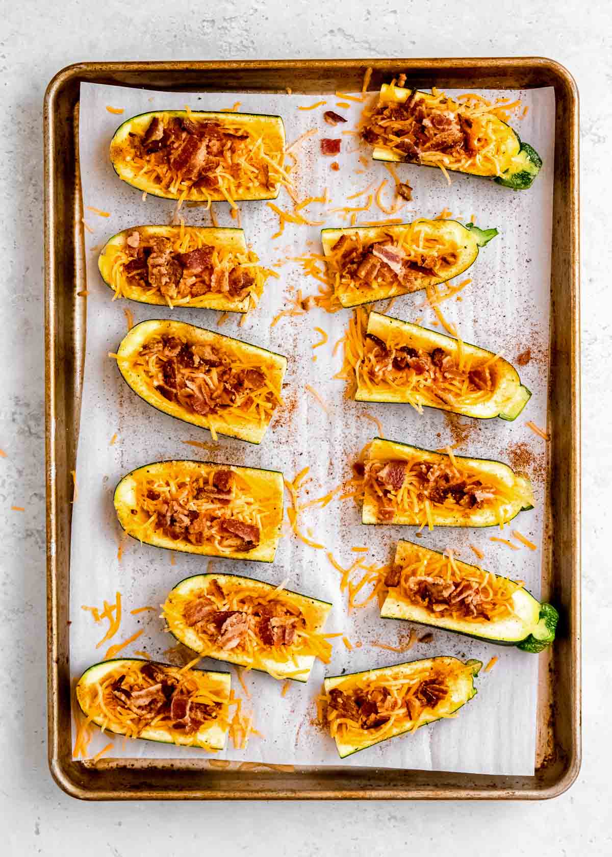 loaded zucchini skins being garnished with bacon on sheet pan