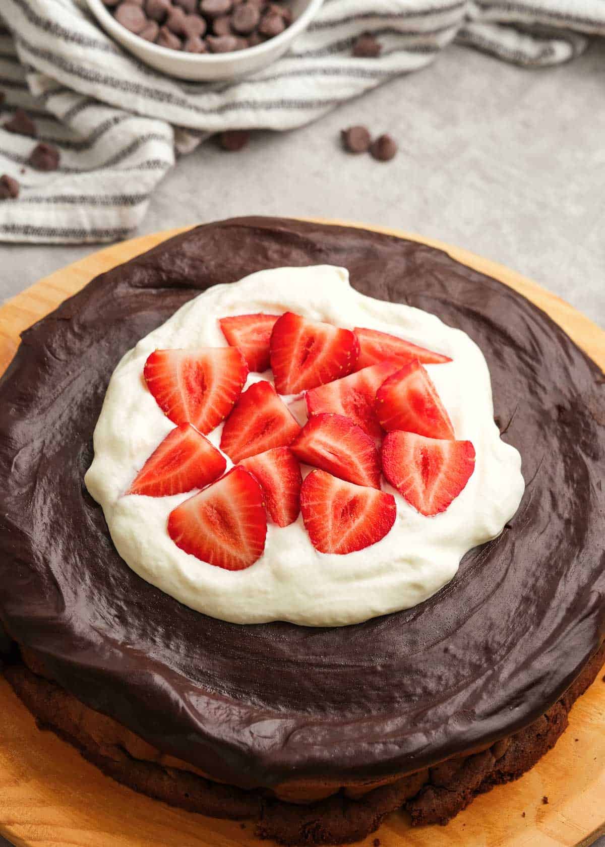 flourless cake on cutting board after topping with whipped cream and strawberries