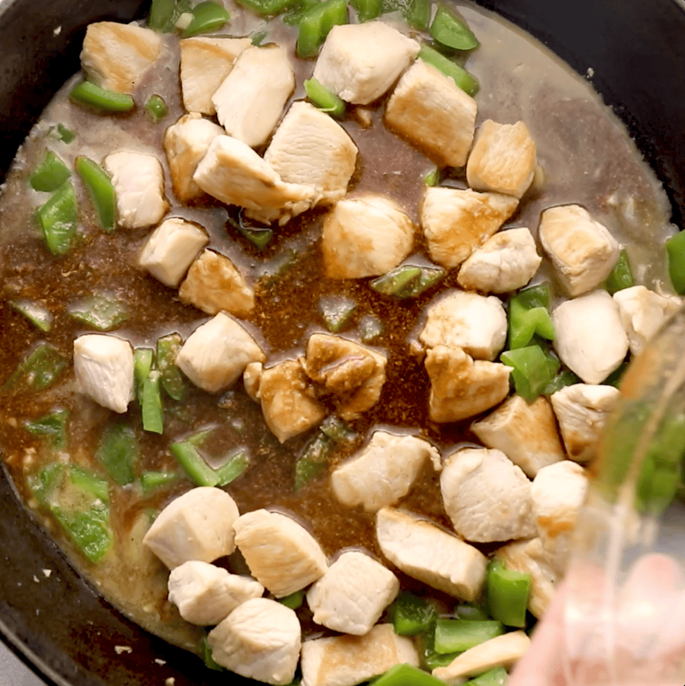 Asian sauce being added to skillet with chicken and peppers