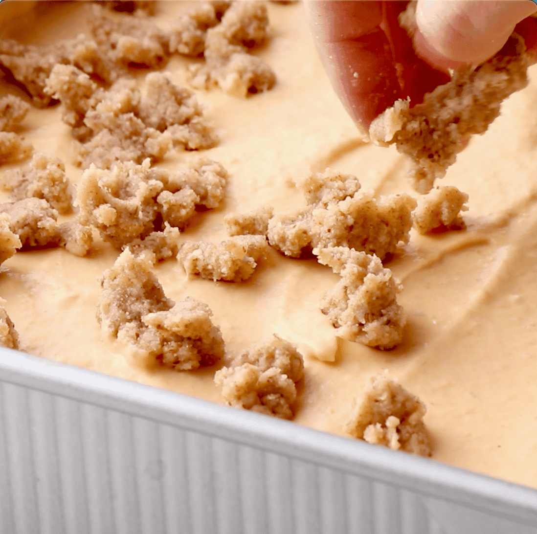 crumble topping being added to cheesecake bars prior to baking