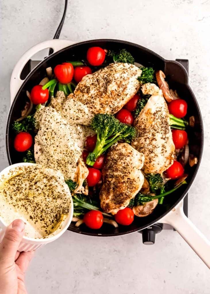 pesto being added to chicken and veggies in cast iron skillet