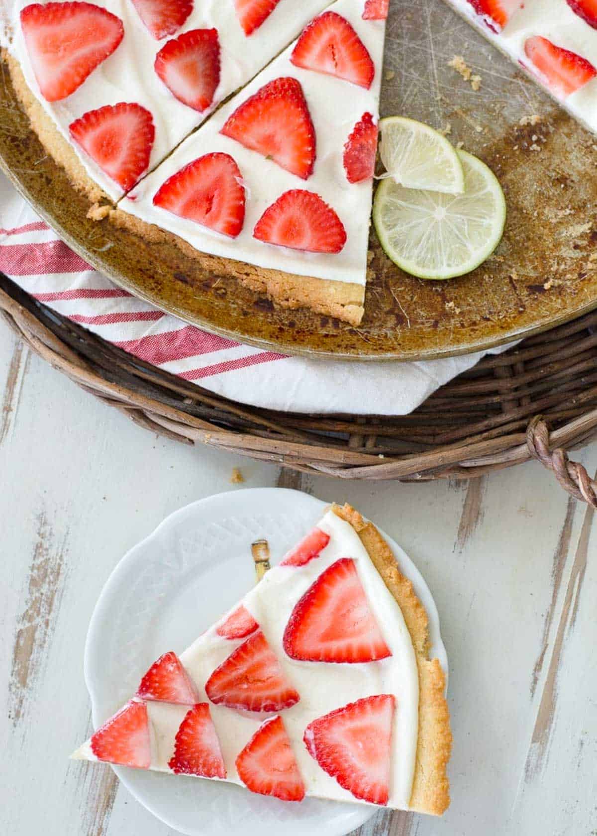 one slice of strawberry fruit pizza on a white plate with the rest of pizza next to it on pizza pan