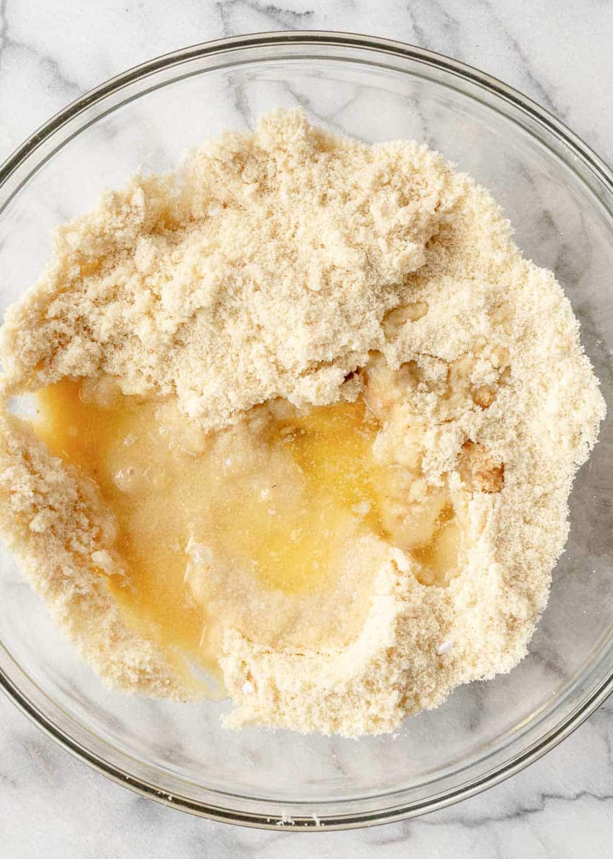 melted butter being added to crust ingredients in clear mixing bowl