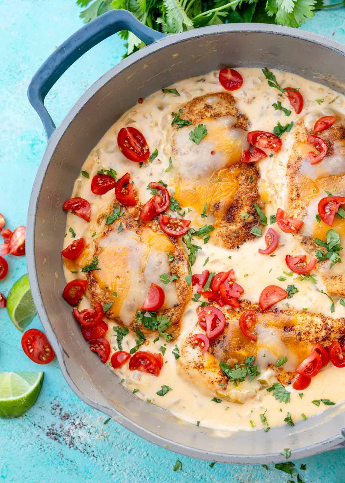 A skillet full of green chili chicken garnished with tomatoes and herbs
