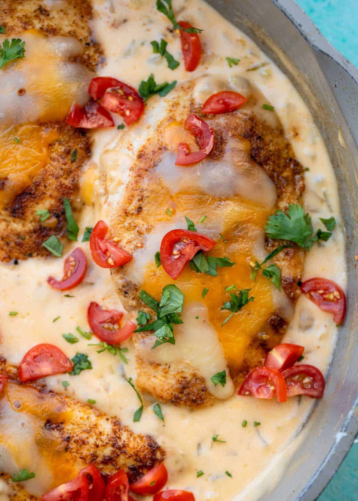 Juicy chicken topped with melty cheese and in a creamy green chili sauce, garnished with fresh herbs and diced tomatoes