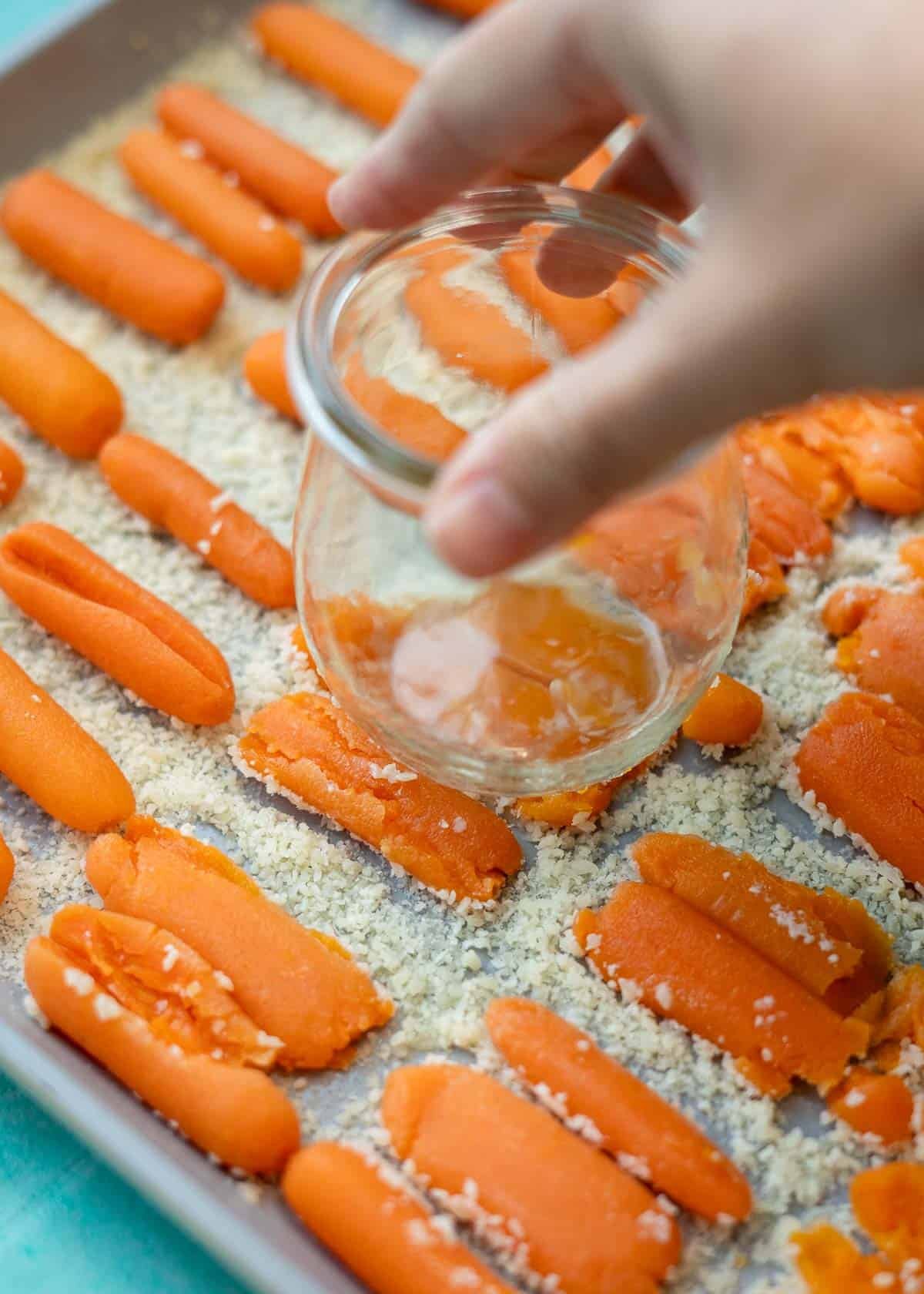 carrots being smashed with jar on sheet pan