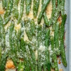 close, overhead image of smashed, cheesy green beans on baking sheet