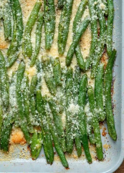 close, overhead image of smashed, cheesy green beans on baking sheet