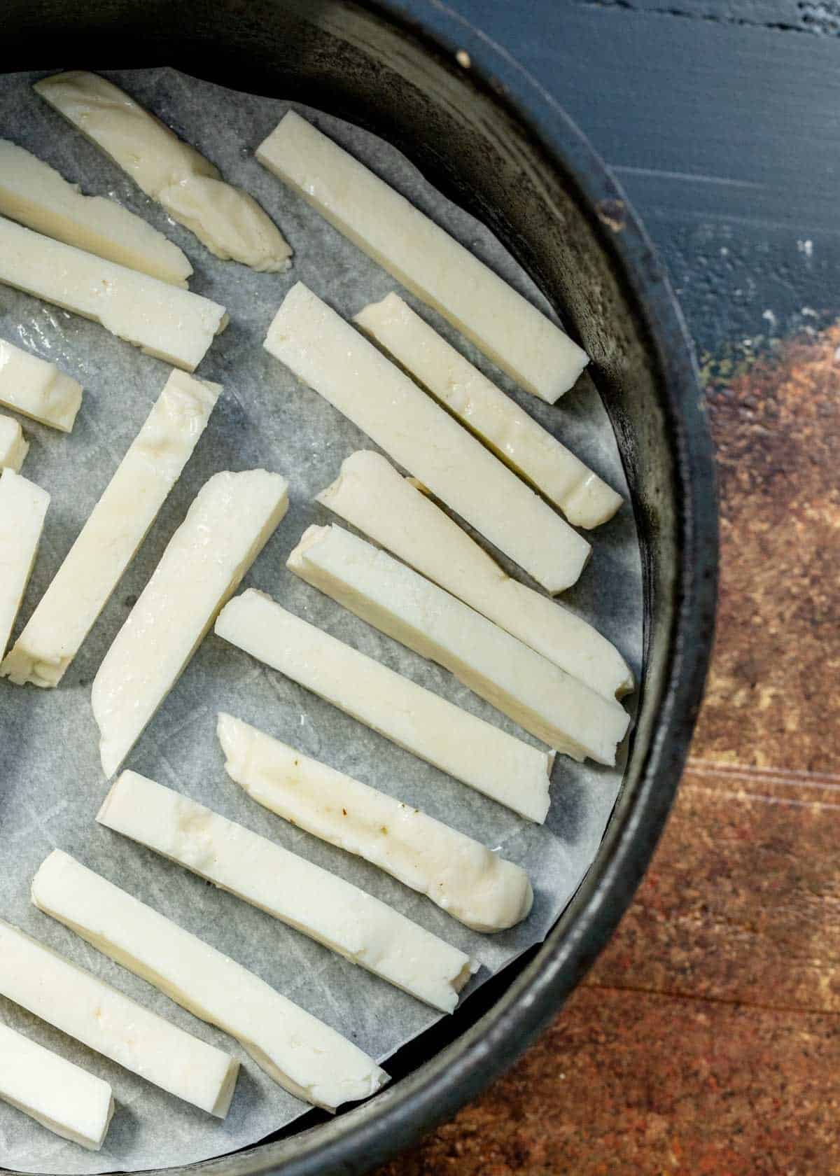 overhead image of halloumi cut in fries on parchment paper in air fryer