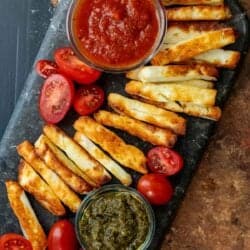 overhead image of halloumi fries lined across black cutting board with marinara in a clear jar