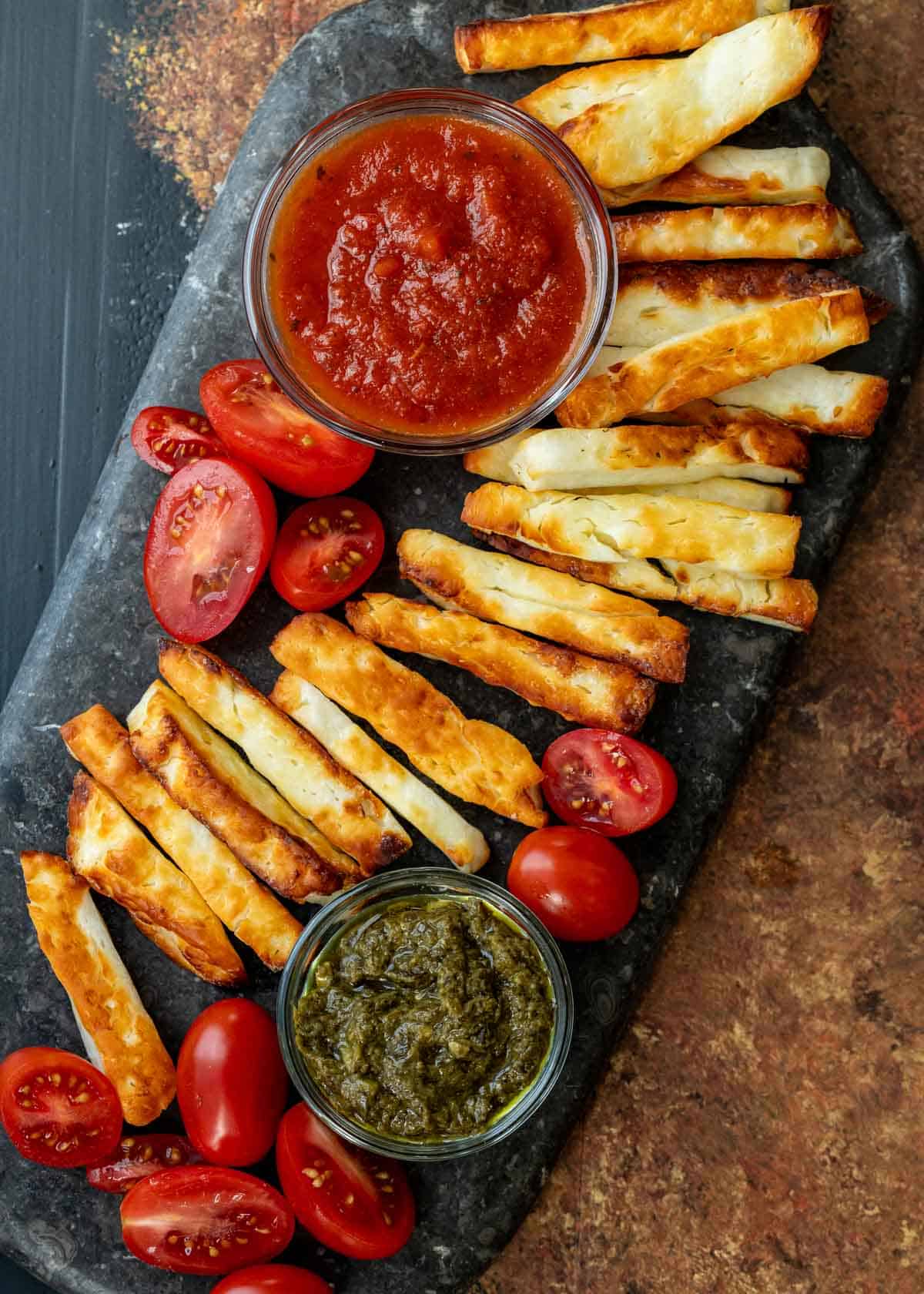 overhead image of halloumi fries lined across black cutting board with marinara in a clear jar