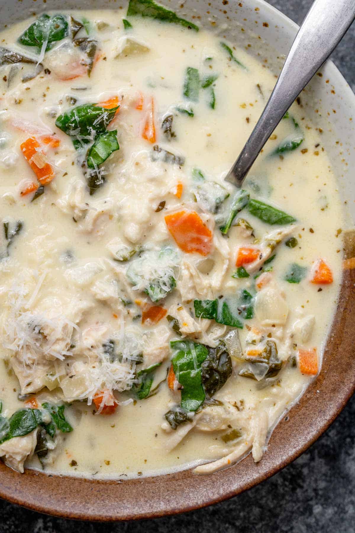 overhead image of chicken florentine soup in a brown and white bowl with a spoon