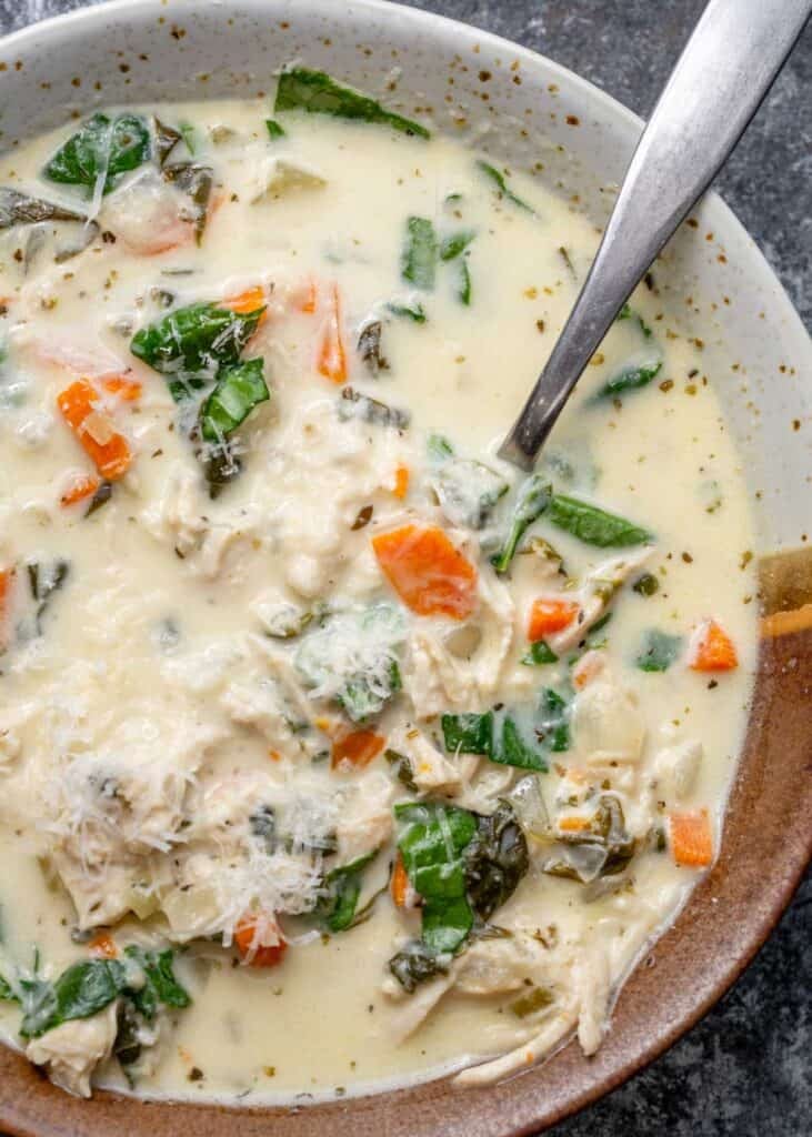 overhead image of chicken florentine soup in a brown and white bowl with a spoon