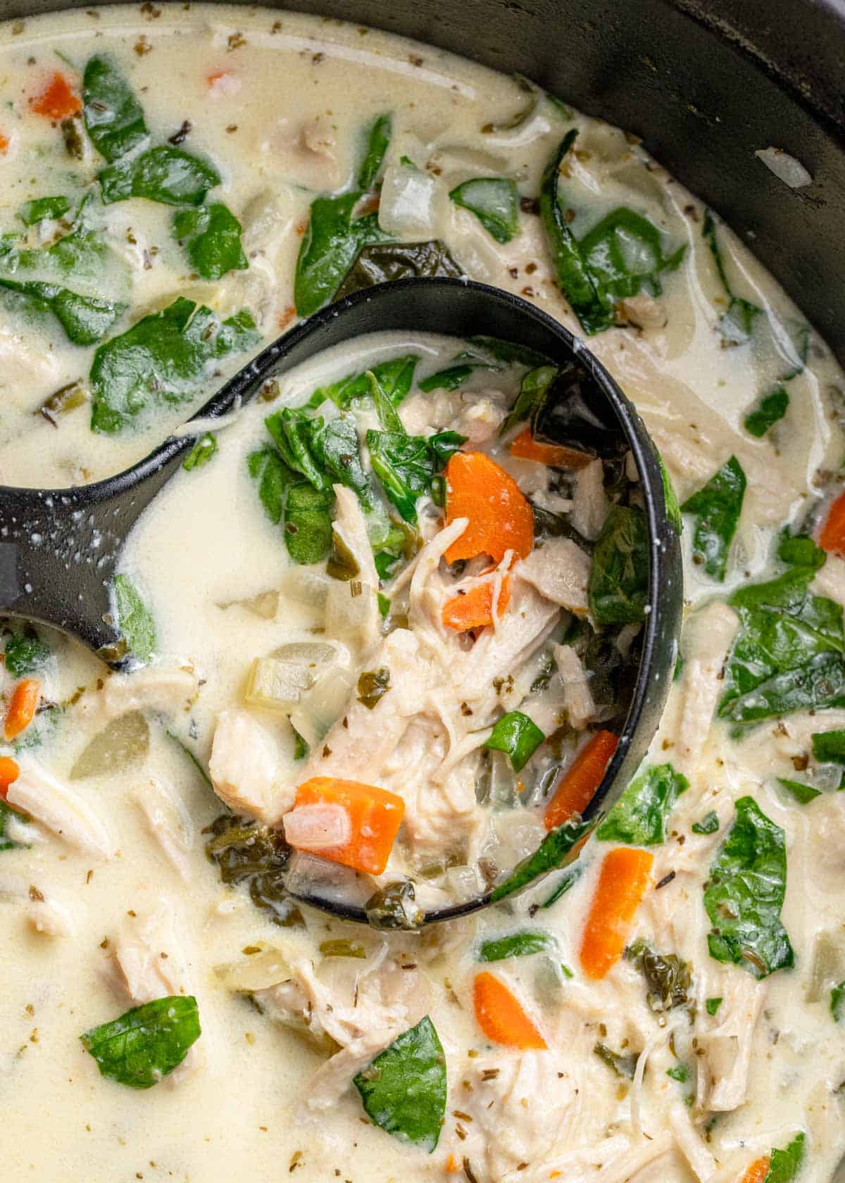 a spoonful of chicken florentine soup being removed from dutch oven