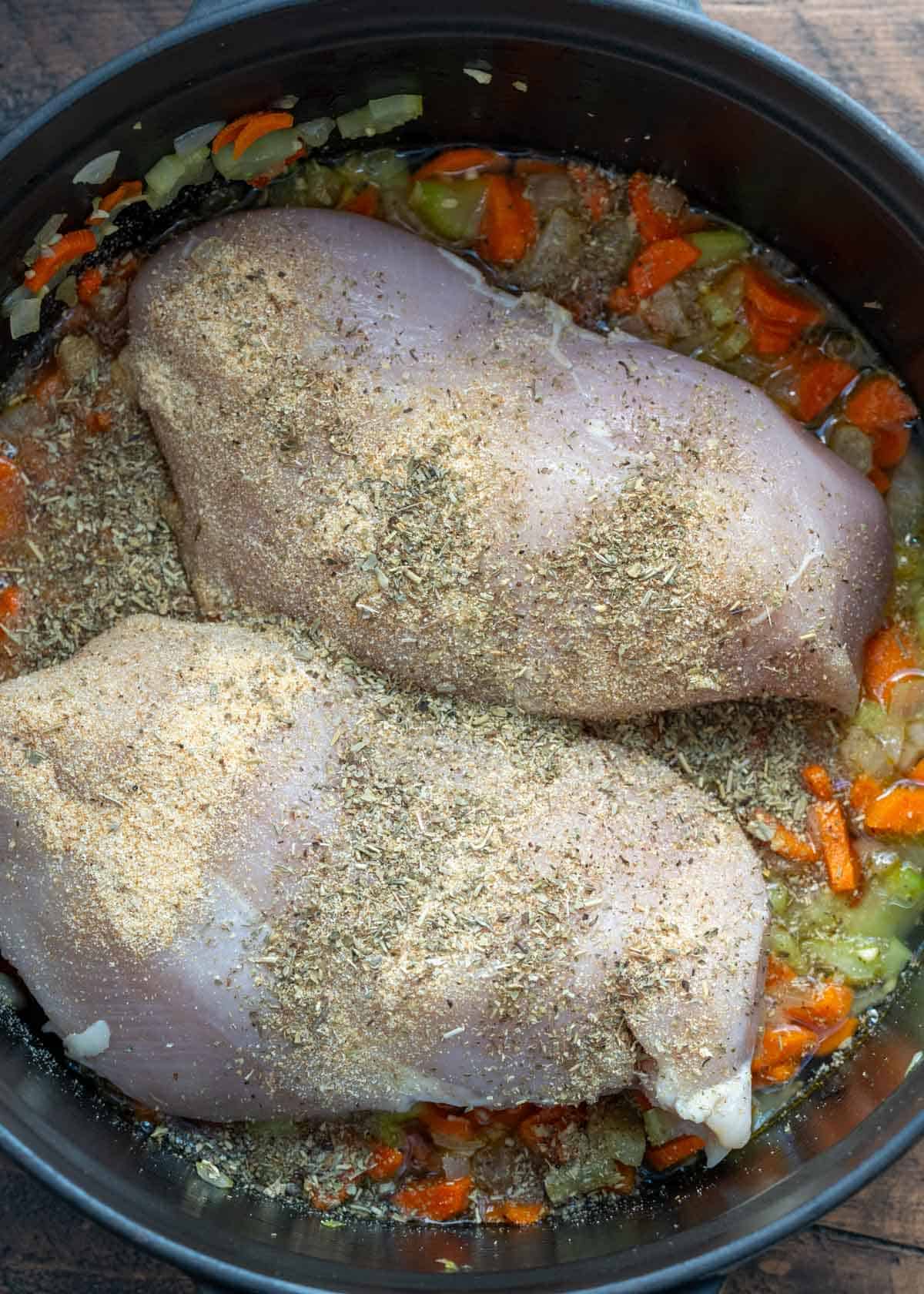 chicken and spices being added to chicken florentine soup in dutch oven