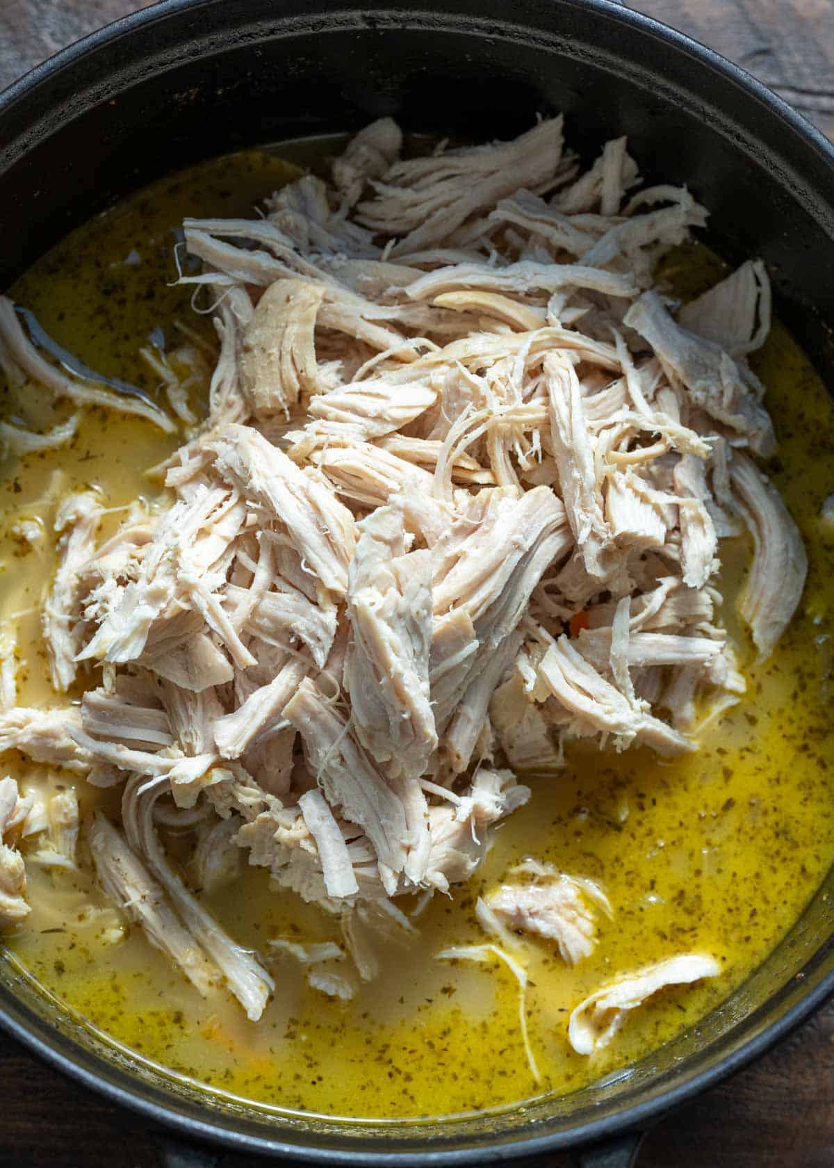 shredded chicken being added back to the chicken florentine soup in dutch oven