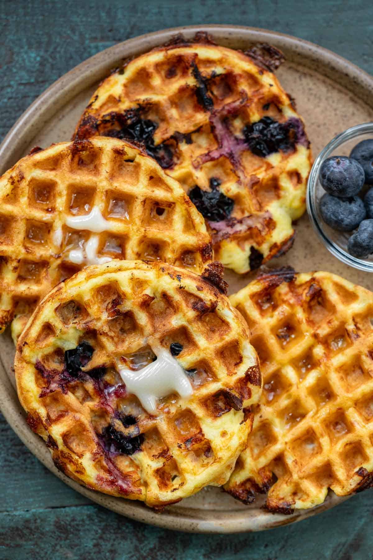 cottage cheese chaffles with blueberries stacked on brown plate