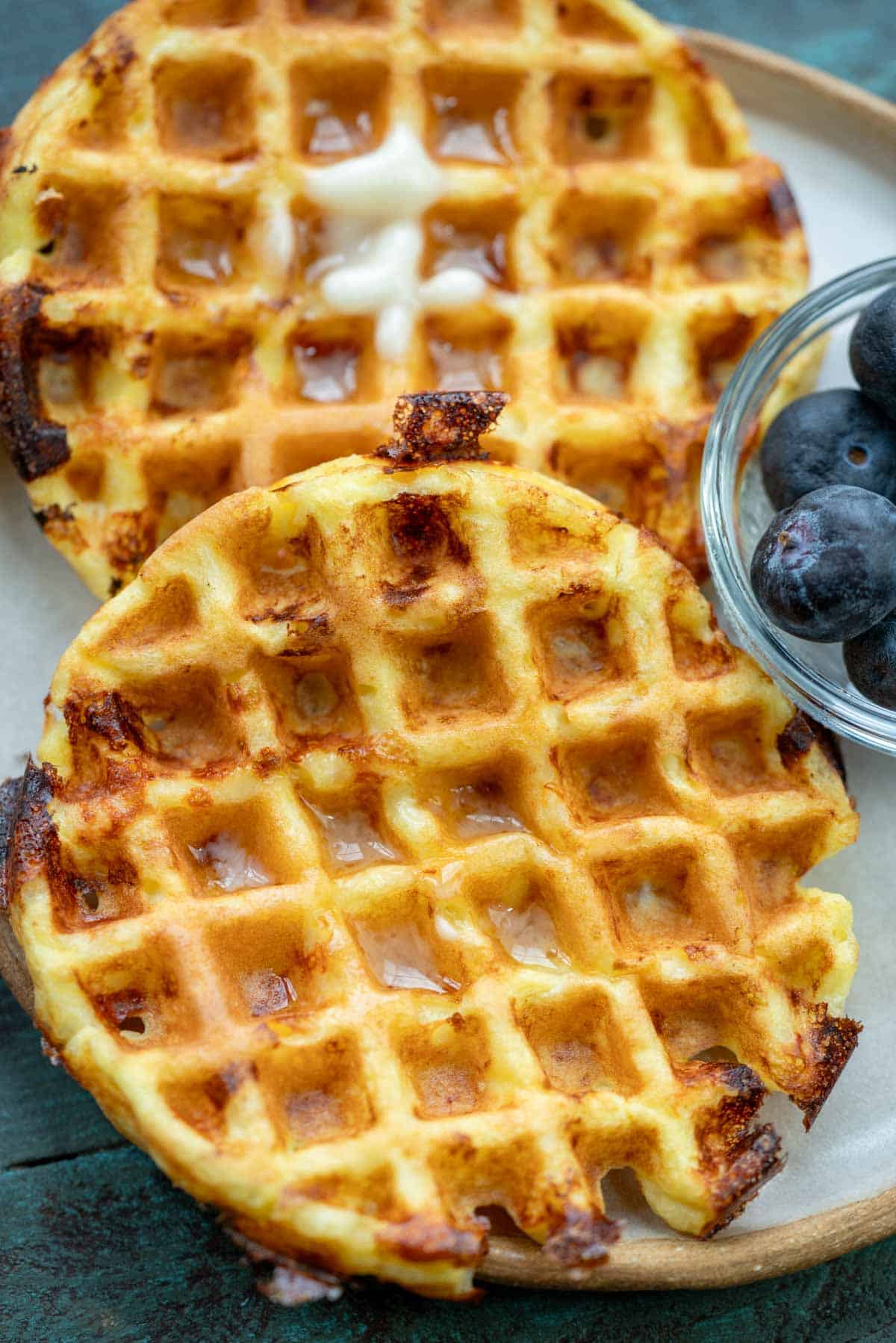 overhead image of cottage cheese chaffles stacked with blueberries in clear bowl