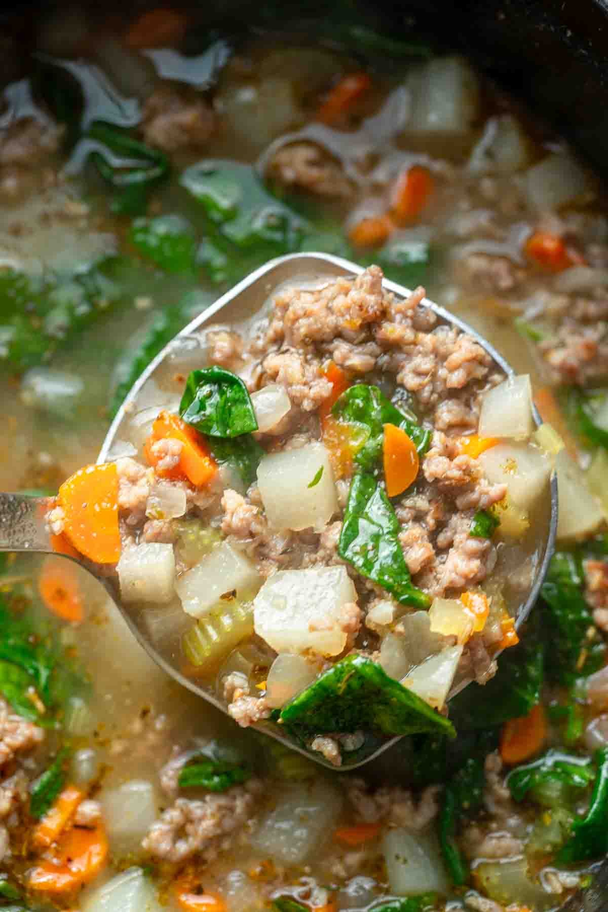 a spoonful of Italian sausage soup being removed from the dutch oven