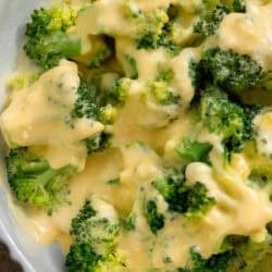 close up image of cheese sauce drizzled over broccoli in a white bowl