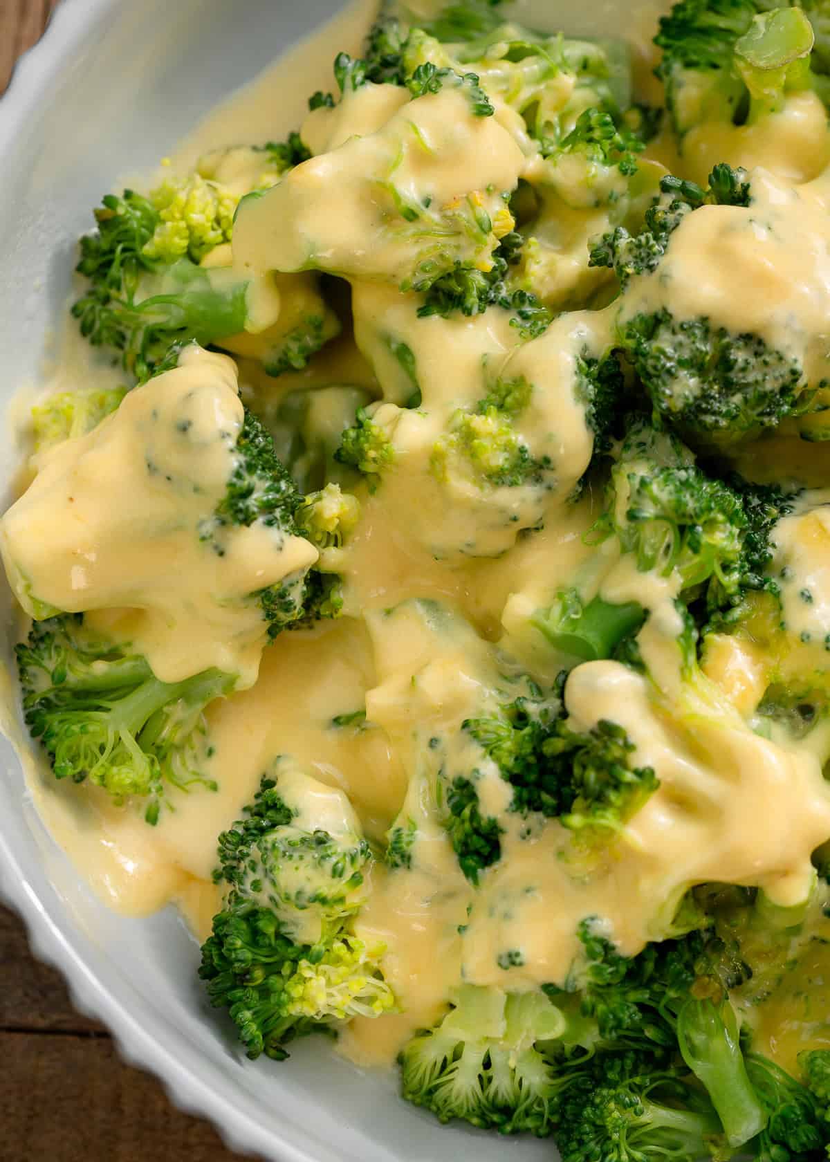 close up image of cheese sauce drizzled over broccoli in a white bowl