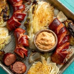 overhead image of sausage, cabbage, and dipping sauce in sheet pan