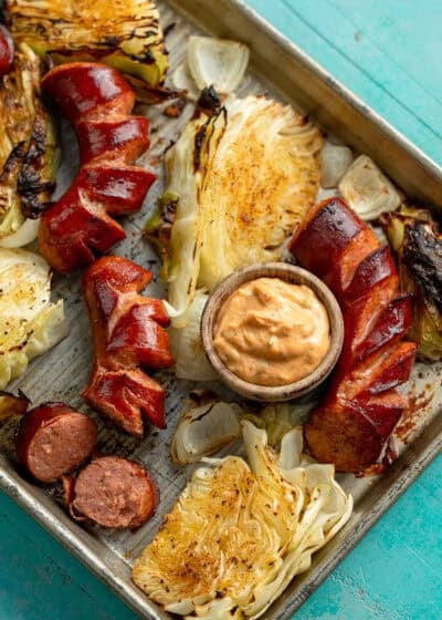 overhead image of sausage, cabbage, and dipping sauce in sheet pan