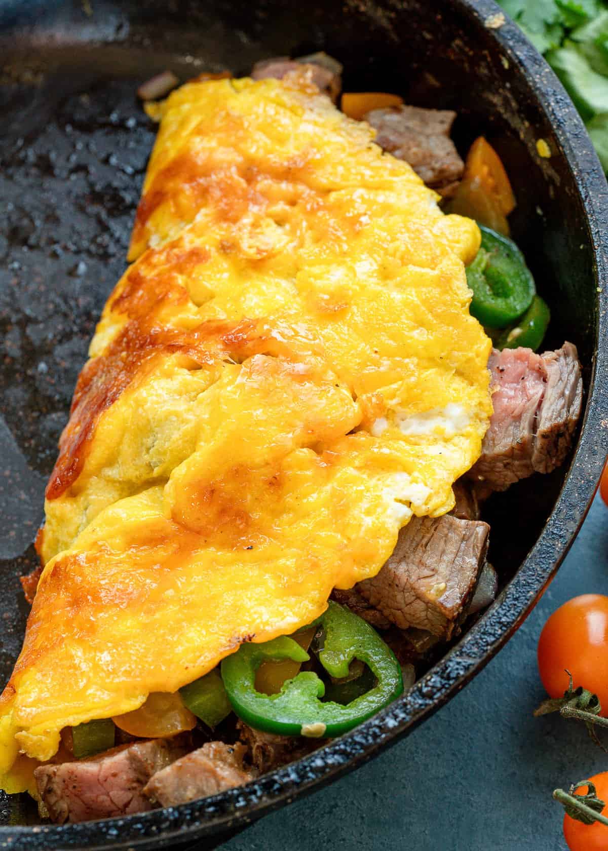 an omelet being folded over in a cast iron skillet with veggies and steak