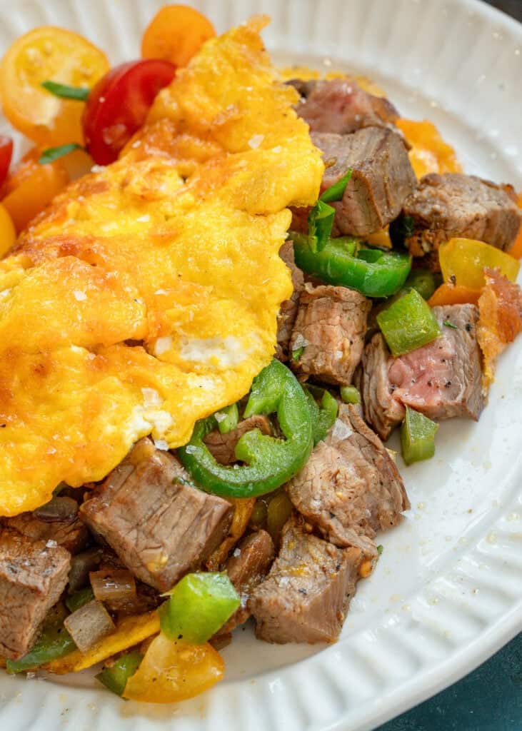overhead, angled image of a steak omelette on a white plate