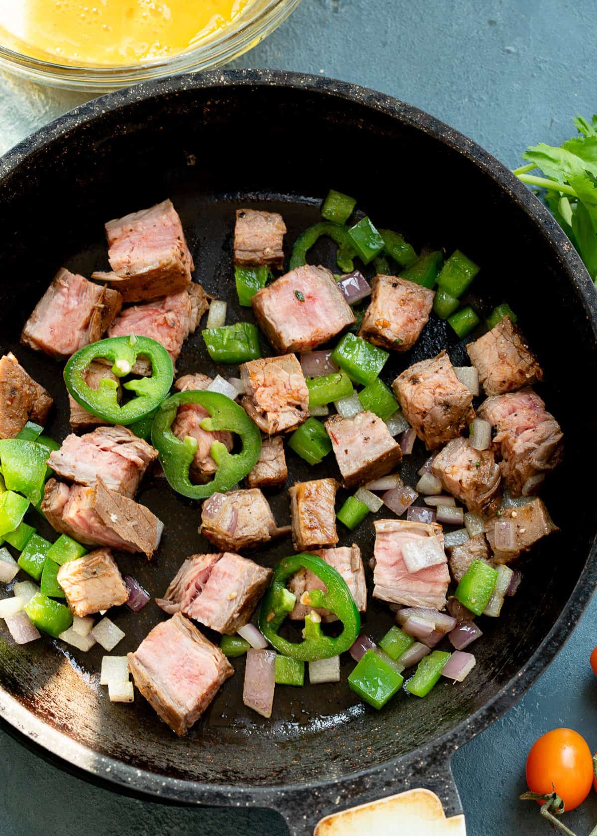 steak and veggies being cooked in cast iron skillet