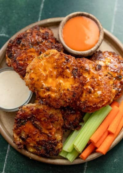 overhead image of buffalo chicken fritters stacked on plate with vegetables