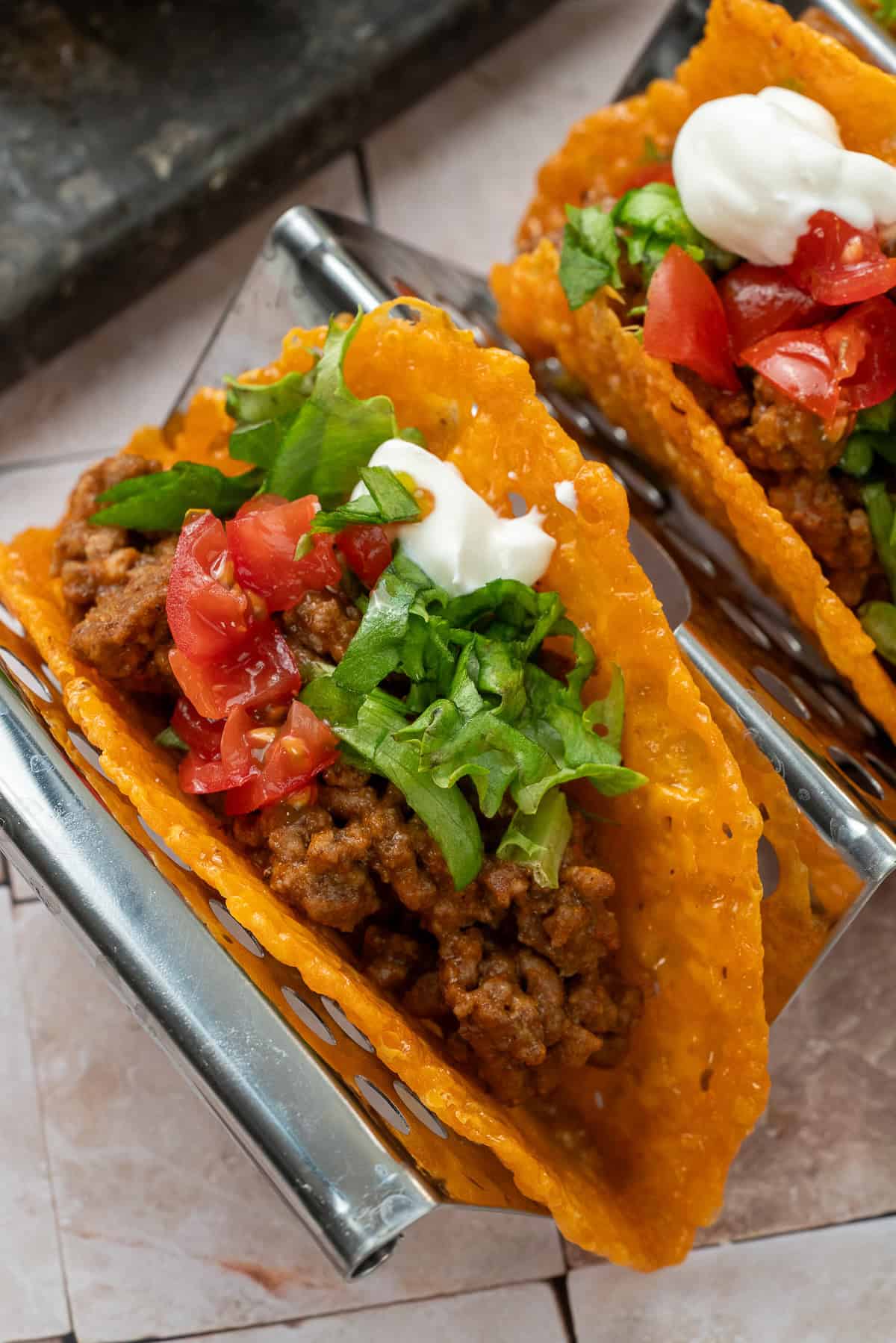 an image of a keto taco being topped with tomatoes and lettuce on a taco rack