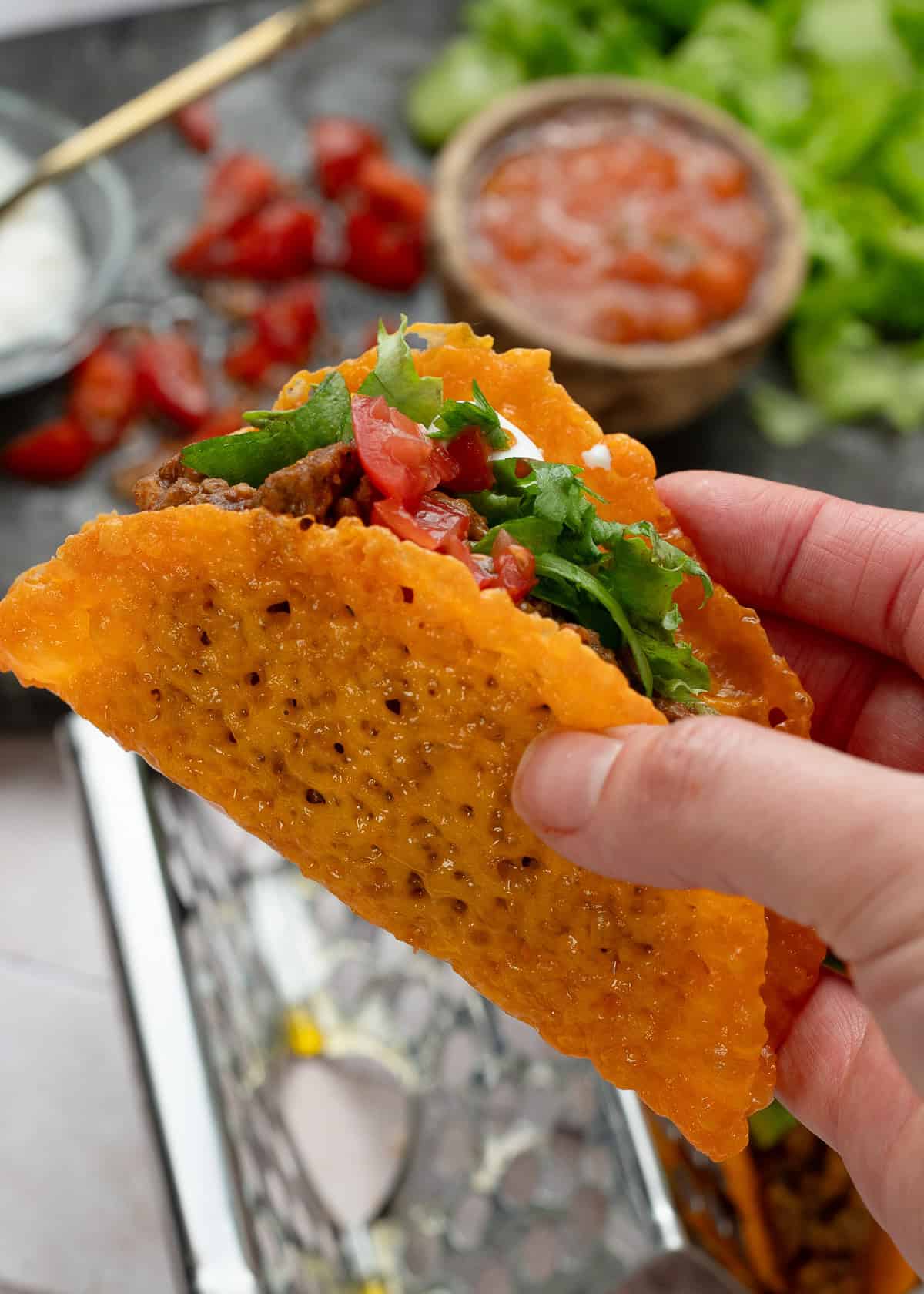 a keto taco being help up close to the camera with additional ingredients in the background