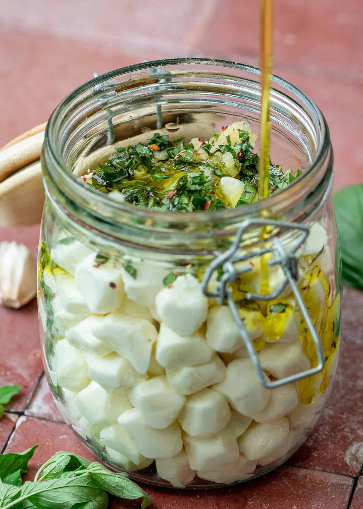 olive oil being drizzled into jar with mozzarella pearls