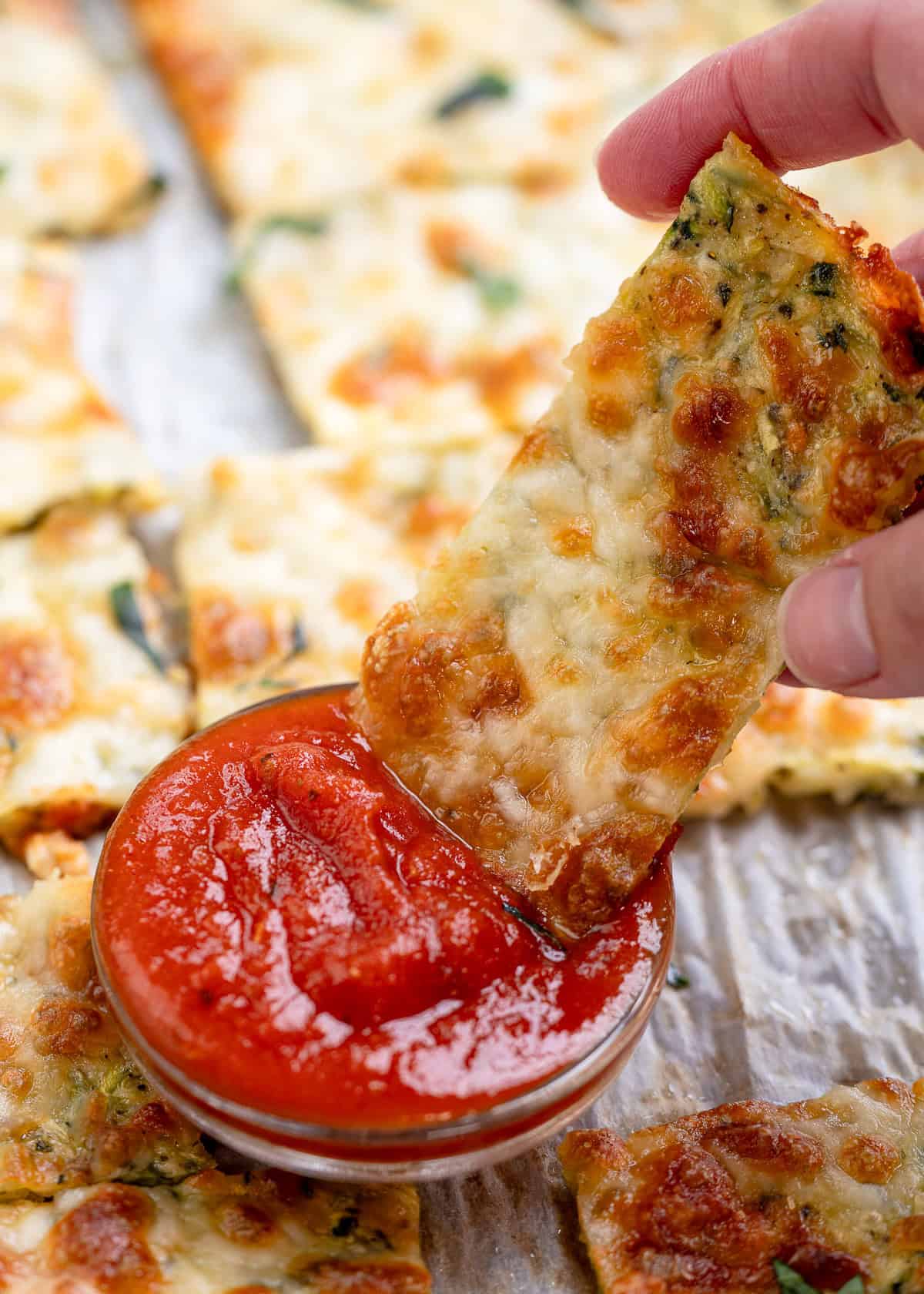 a zucchini breadstick being dipped in marinara sauce