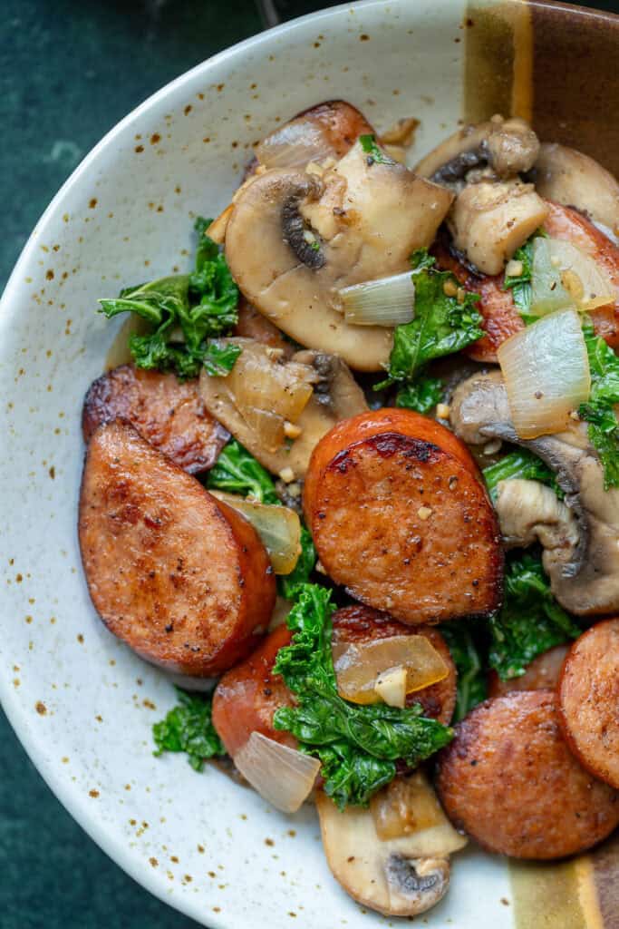 overhead image of andouille sausage and vegetables in a white and brown bowl