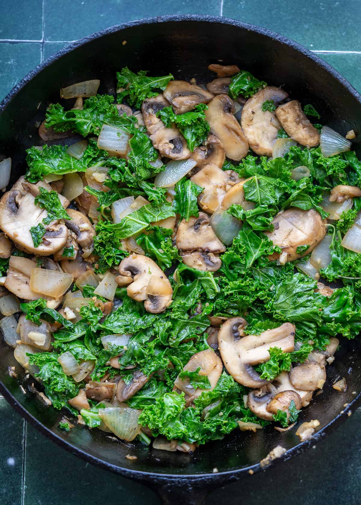 kale being added to cast iron skillet with other veggies in cast iron skillet