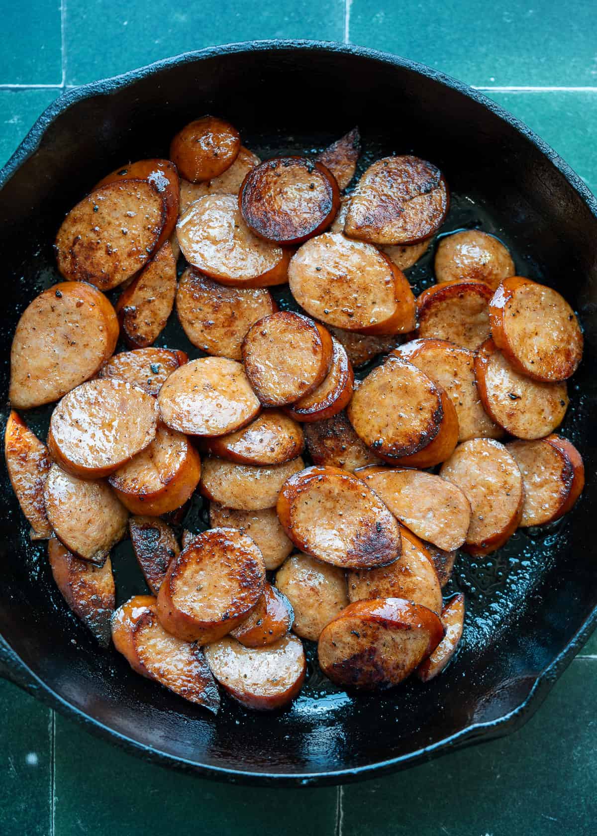 andouille sausage being browned in a cast iron skillet