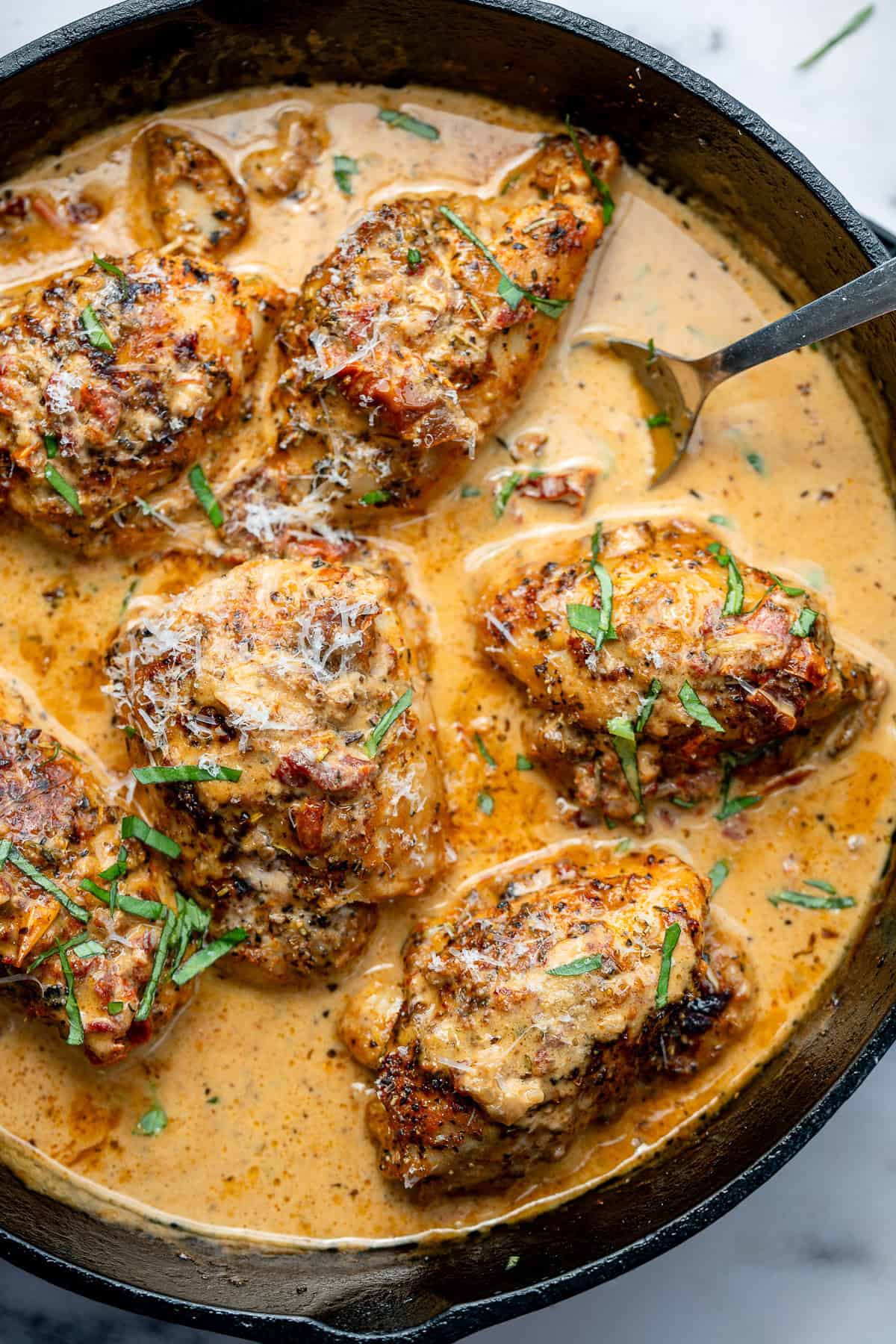 overhead image of multiple cooked tuscan chicken thighs in a cast iron skillet with a creamy sauce