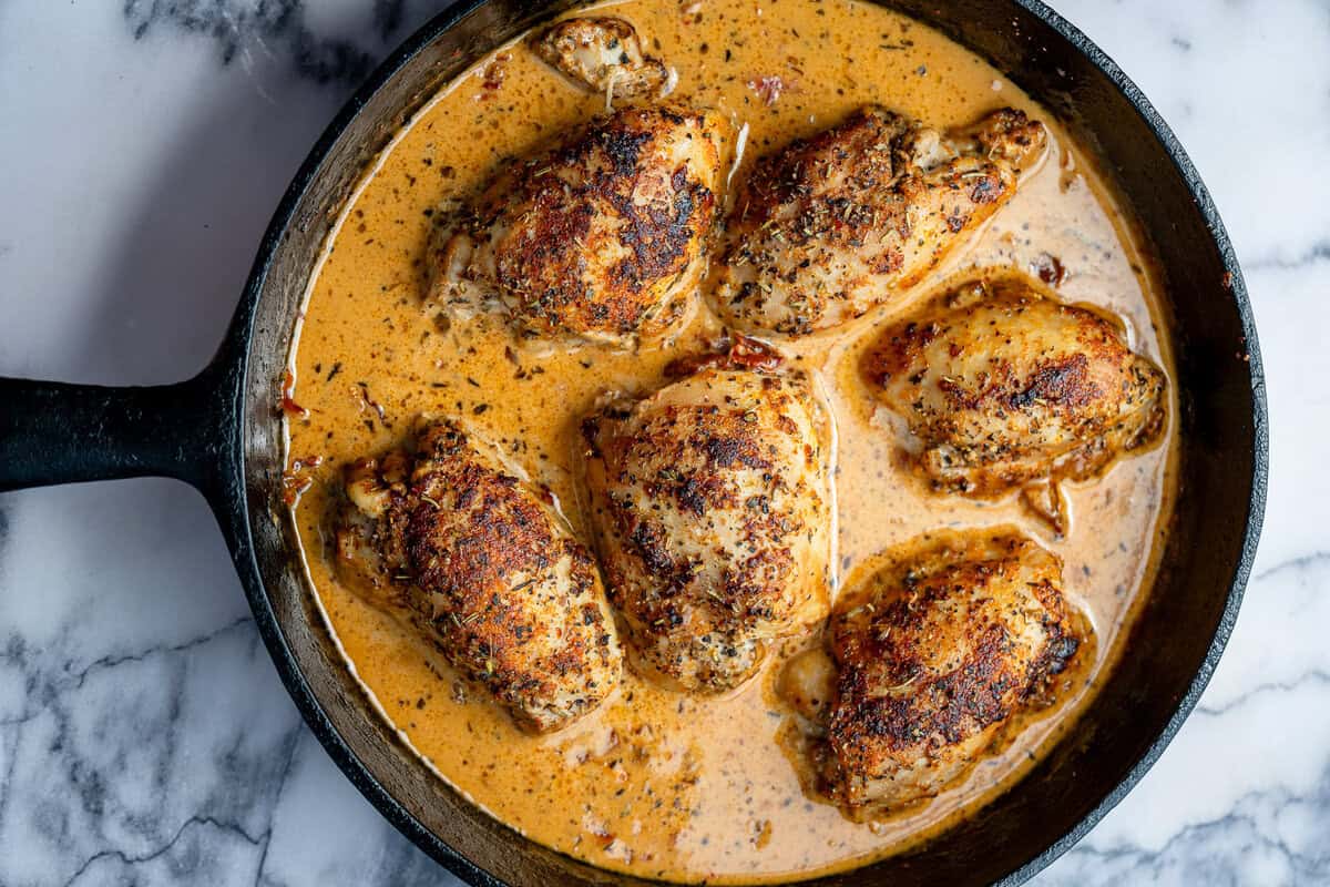 chicken thighs being added back to a cast iron skillet with the Tuscan sauce