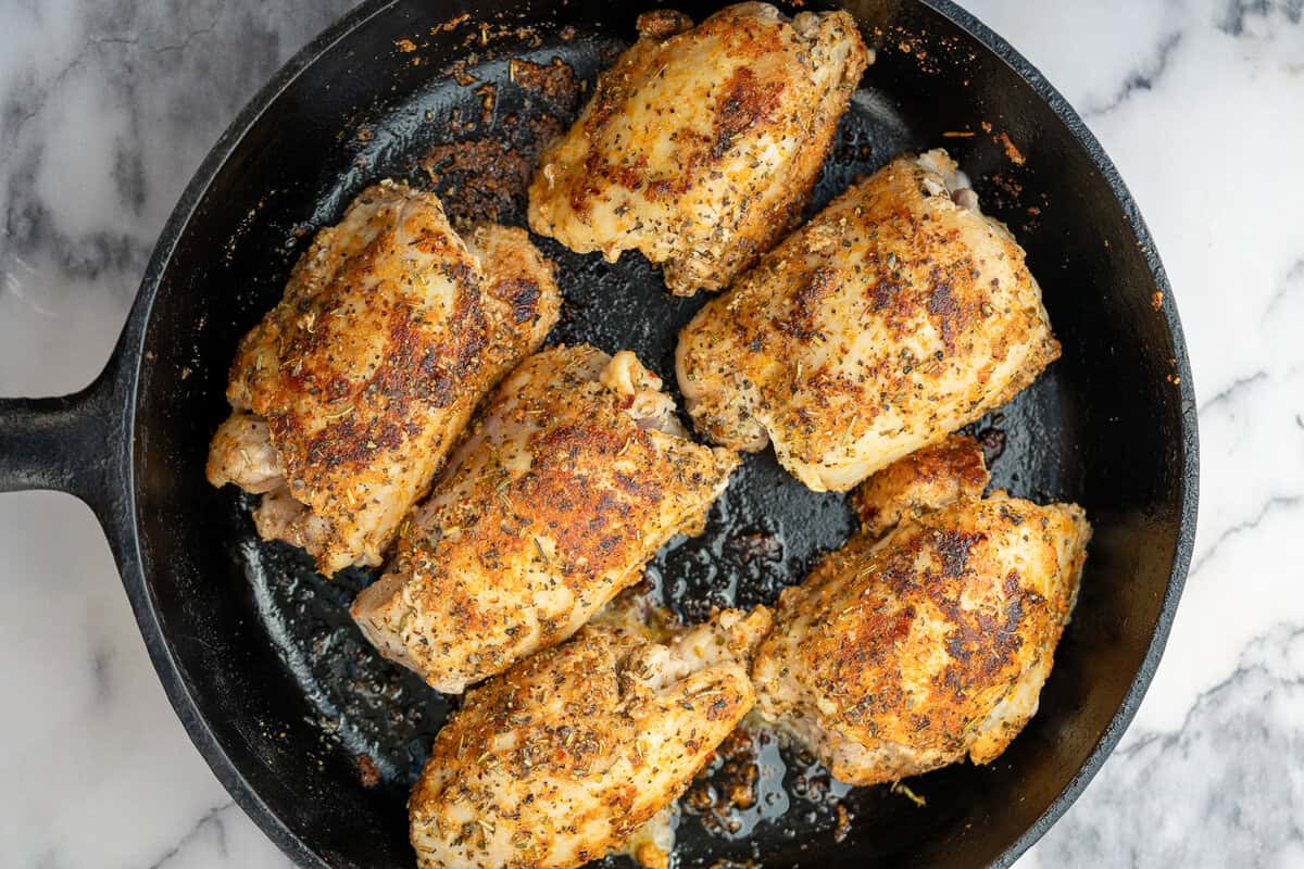chicken thighs being browned in a cast iron skillet